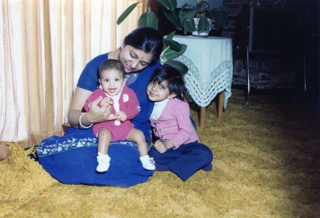 Manjula sitting on the floor with her two young children, smiling