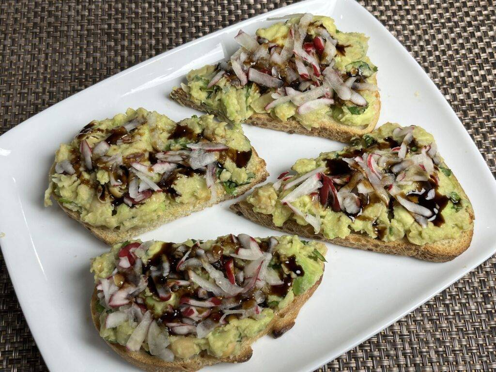 A slice of toast topped with mashed avocado and chickpeas, garnished with herbs