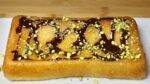 A rectangular Gulab Jamun Cake topped with a drizzle of chocolate syrup and garnished with crushed pistachios.