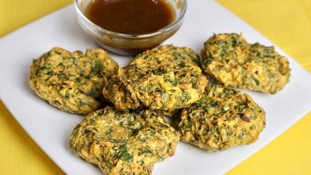 Six palak pakoras served with a bowl of tamarind chutney on a white plate.