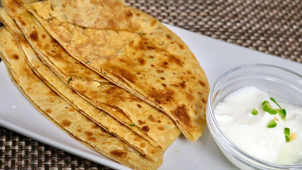 Close-up view of Sattu Paratha served with a bowl of yogurt garnished with green chilies.