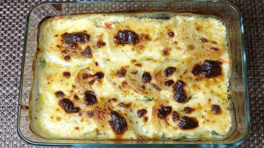 A glass baking dish filled with golden brown scalloped potatoes topped with a creamy, bubbly cheese sauce.