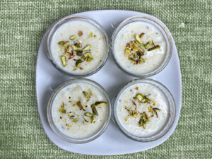 A top-down view of three bowls of rice pudding garnished with sliced pistachios, placed on a green textured surface.